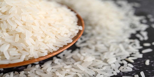 Milled rice in a bowl and a wooden spoon on the black cement floor. Selective focus
